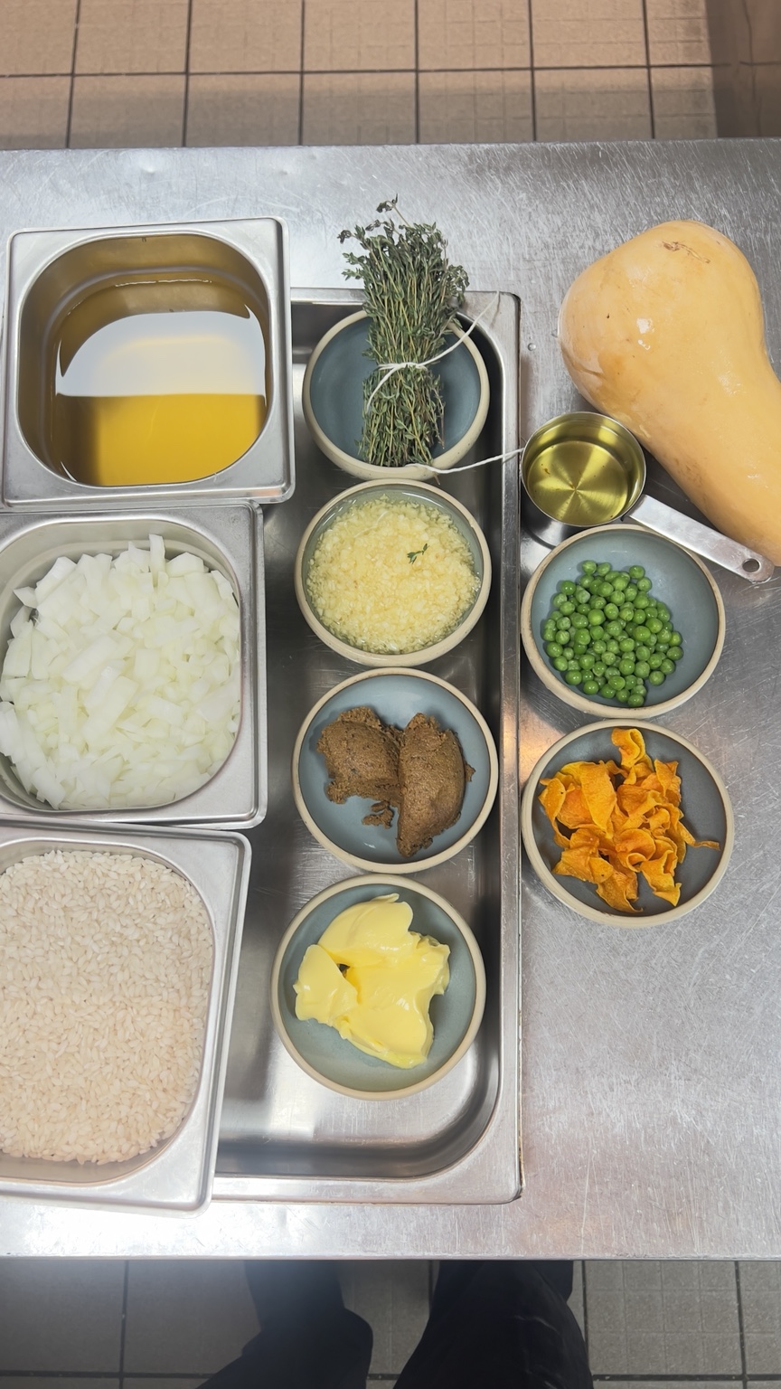 Risotto rice, diced onion, herbs, peas, butter, Parmesan and butternut squash arranged in a professional kitchen