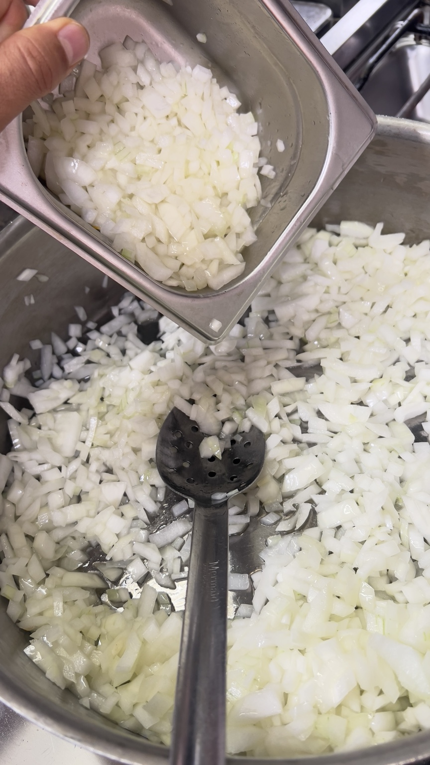 Diced onions being gently sautéed in a wide professional cooking pan